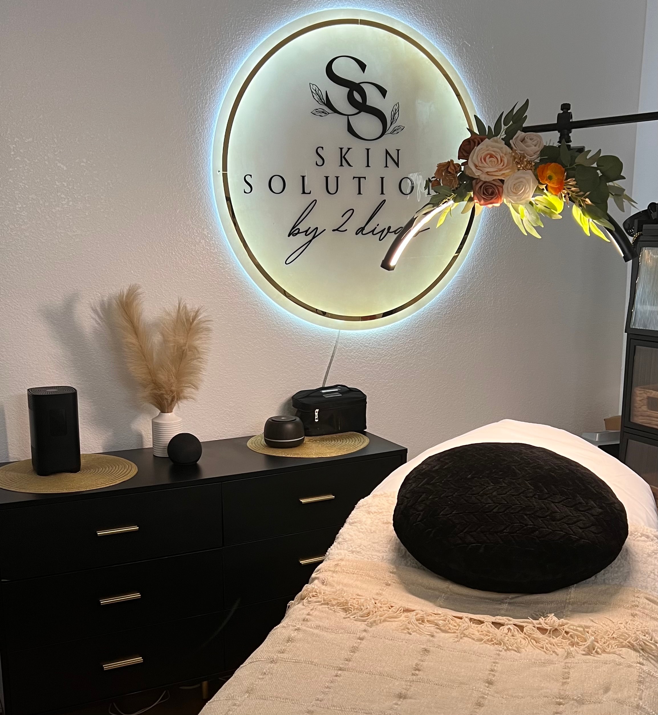 Skin Solutions by 2 Divas treatment room with glowing sign and floral decor